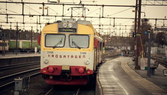 Ett Krösatåg på väg in vid en perrong.